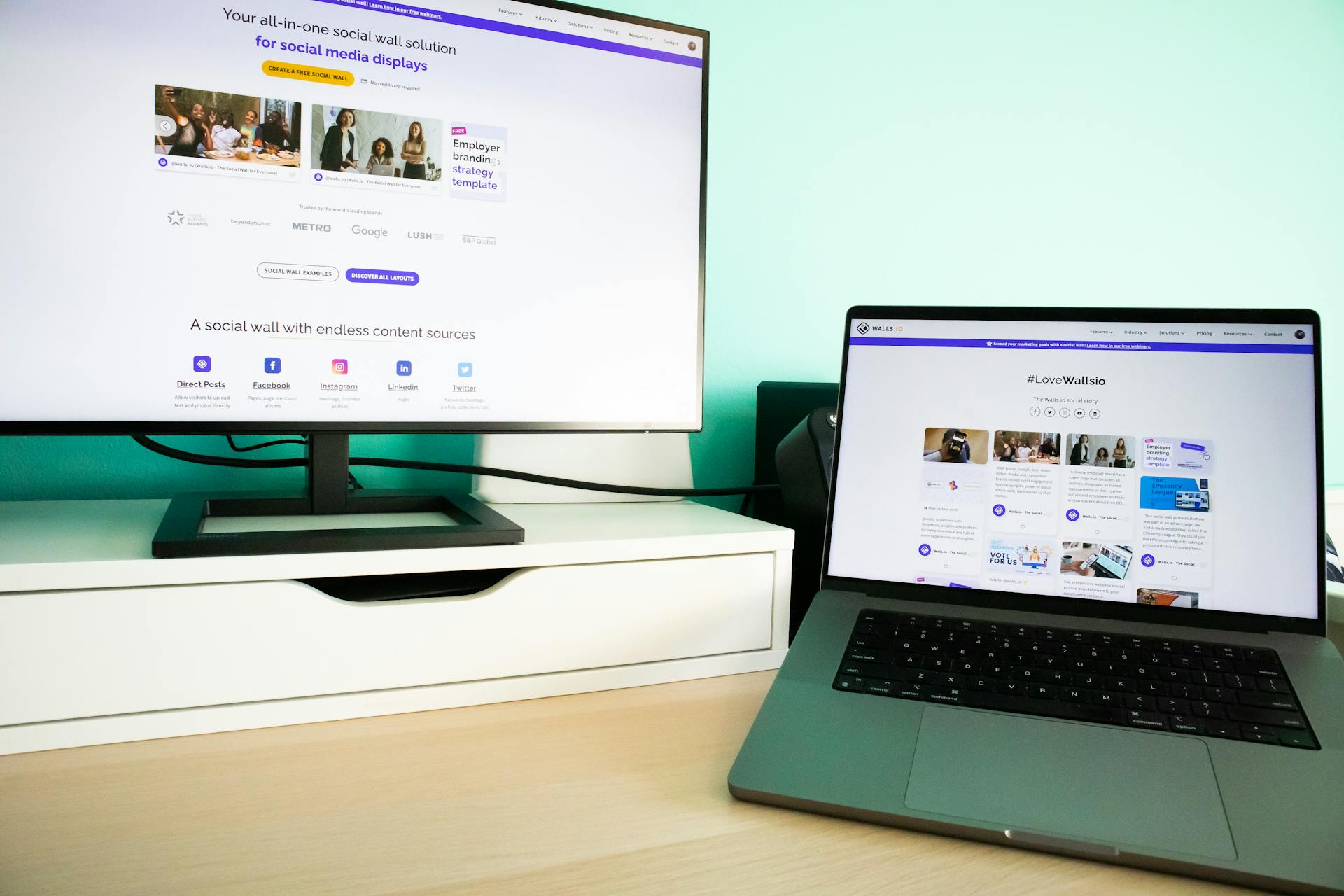 Office desk workspace with a laptop and a monitor displaying a social media wall solution.