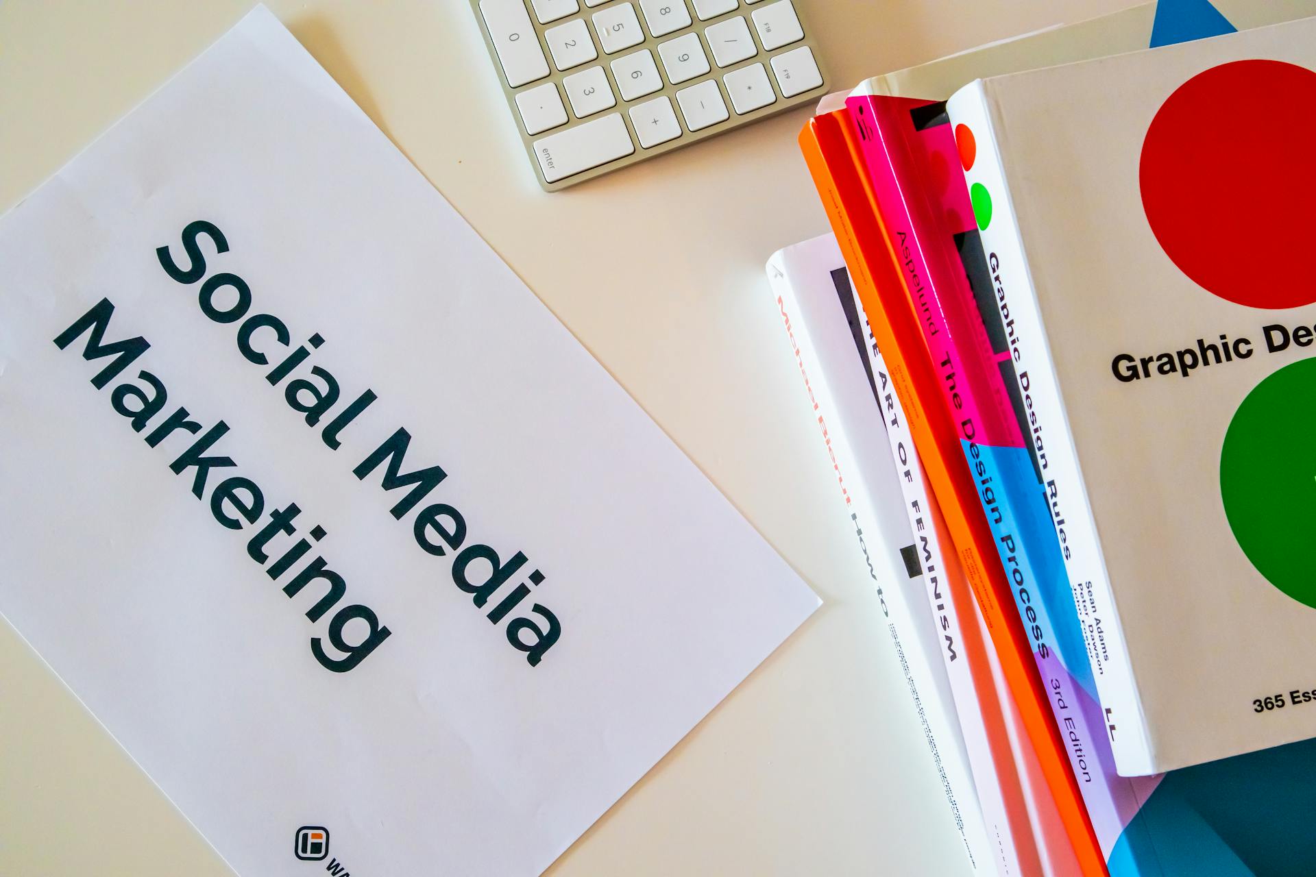 A top view of social media marketing text alongside graphic design books and a keyboard.