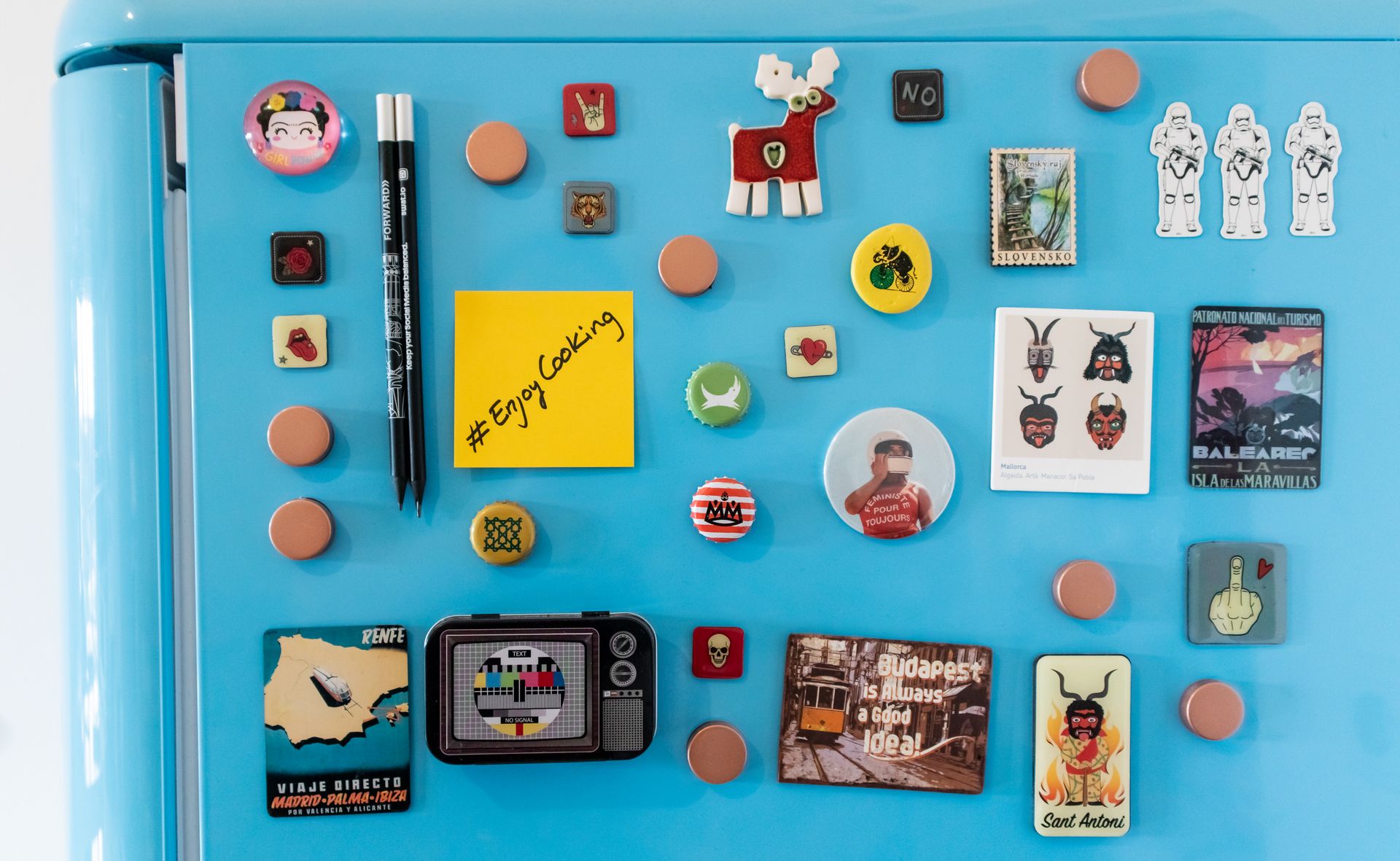 Vibrant collection of refrigerator magnets on a blue fridge, showcasing travel souvenirs.