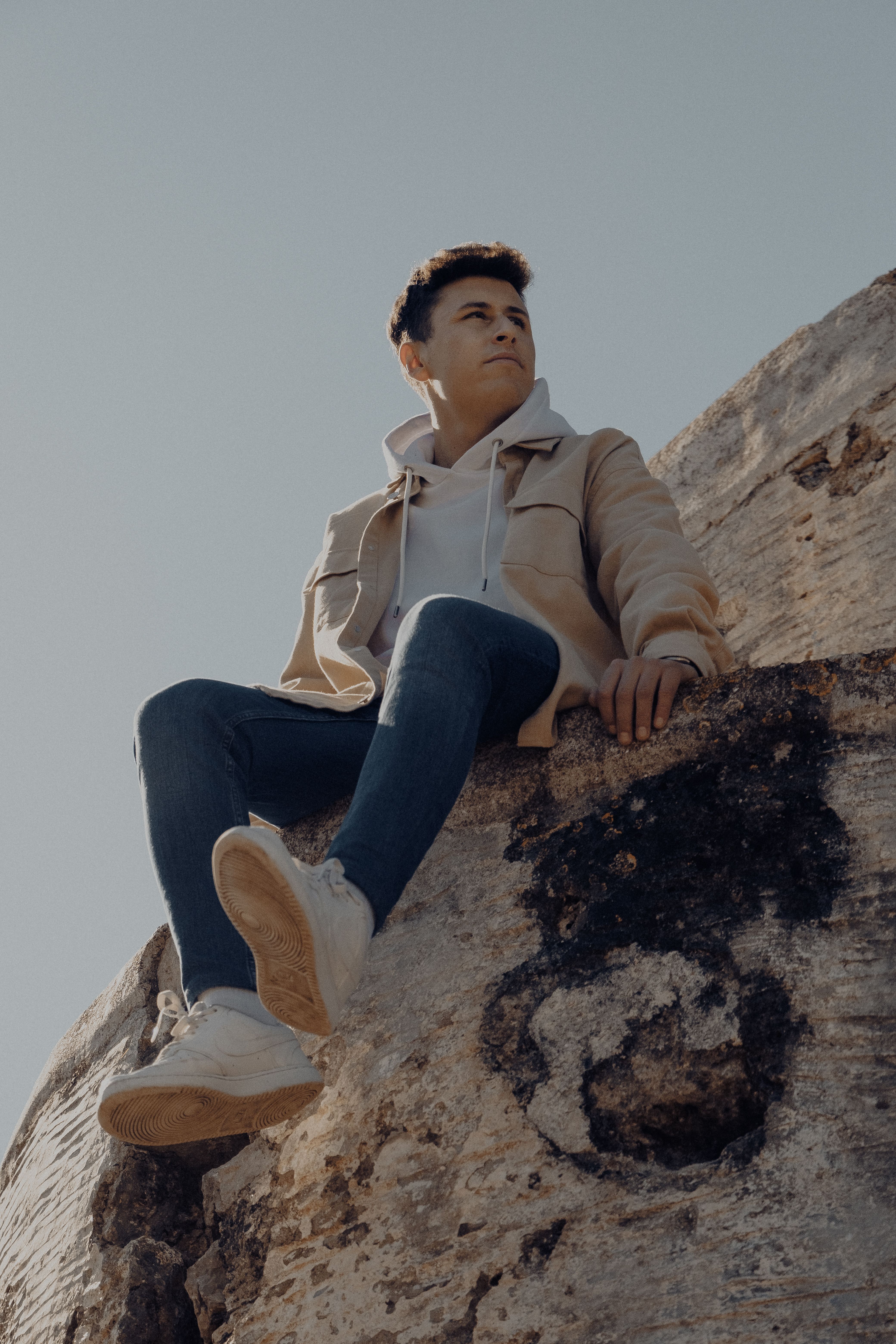 Adult man in casual fashion sitting on a rock under clear sky. Modern and serene outdoor scene.