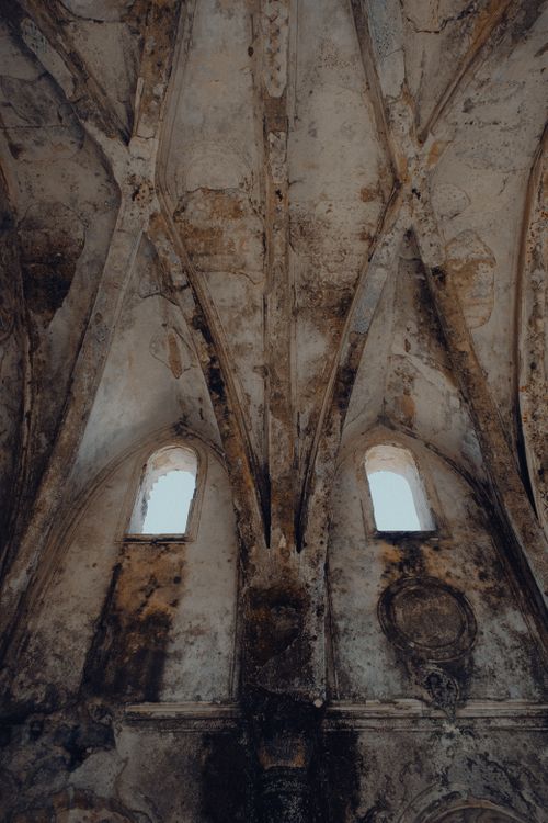 Free A dramatic view of a weathered Gothic church ceiling with intricate arches and two windows. Stock Photo