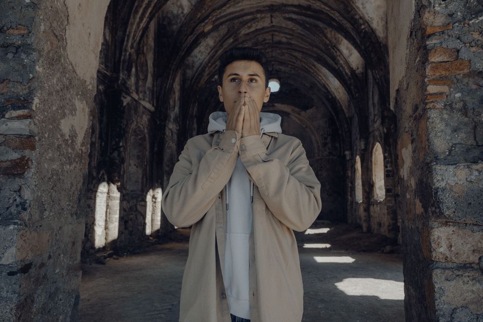 Man wearing casual attire stands thoughtfully in abandoned cathedral ruins.