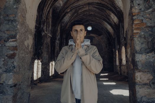 A young man in a hoodie poses thoughtfully in a historic stone arcade with arched ceilings.
