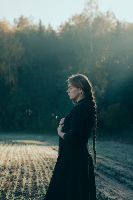 Young woman with braided hair standing in a serene autumn field, embracing nature.
