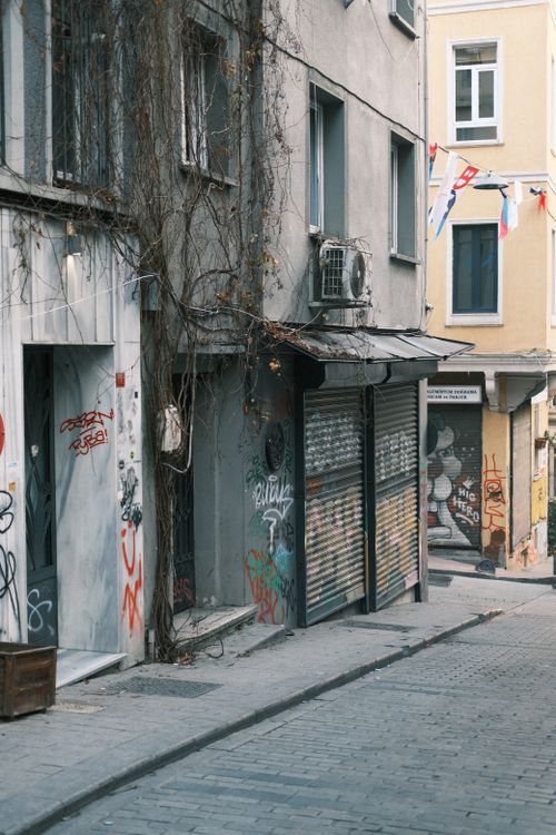 Free A deserted urban alley with graffiti-covered walls, flags, and closed storefronts, capturing a hint of city life. Stock Photo