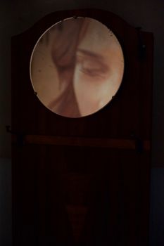 A woman's abstract portrait reflected in a round mirror with artistic lighting.