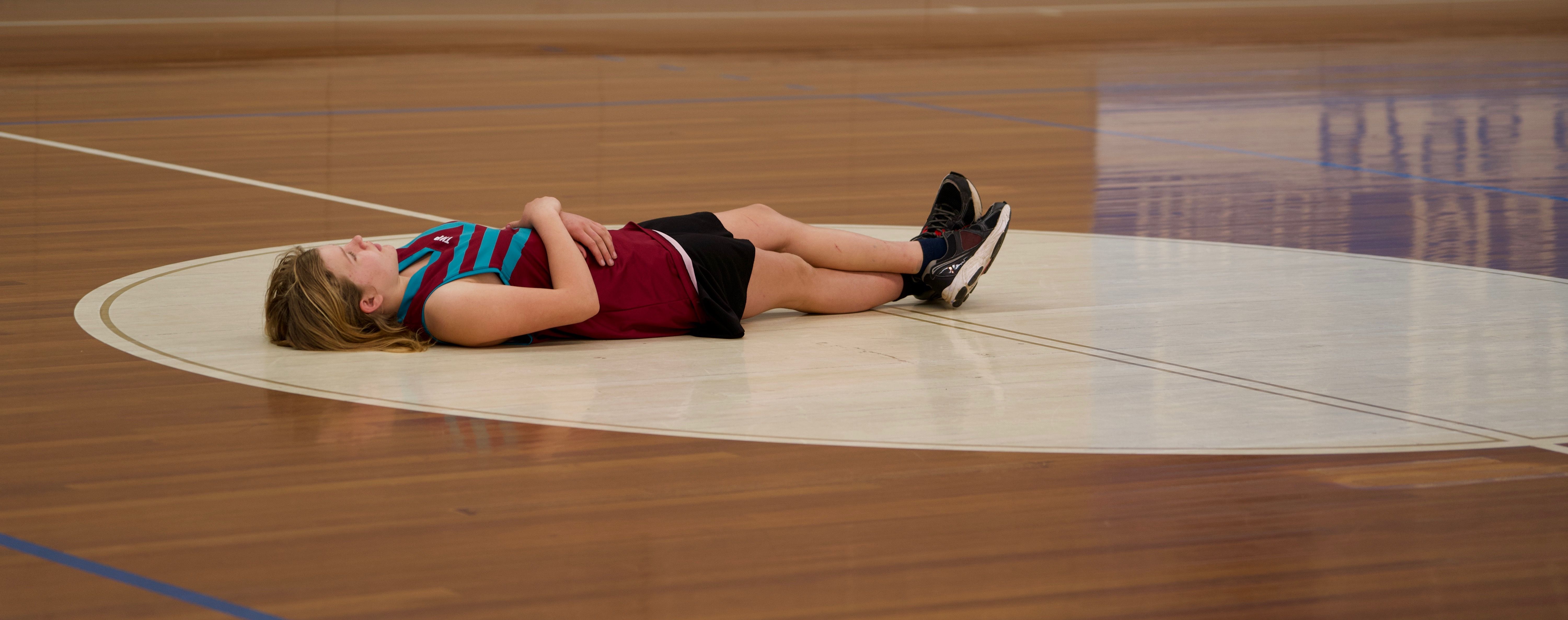 A young female basketball player lies on a court, capturing a moment of rest.