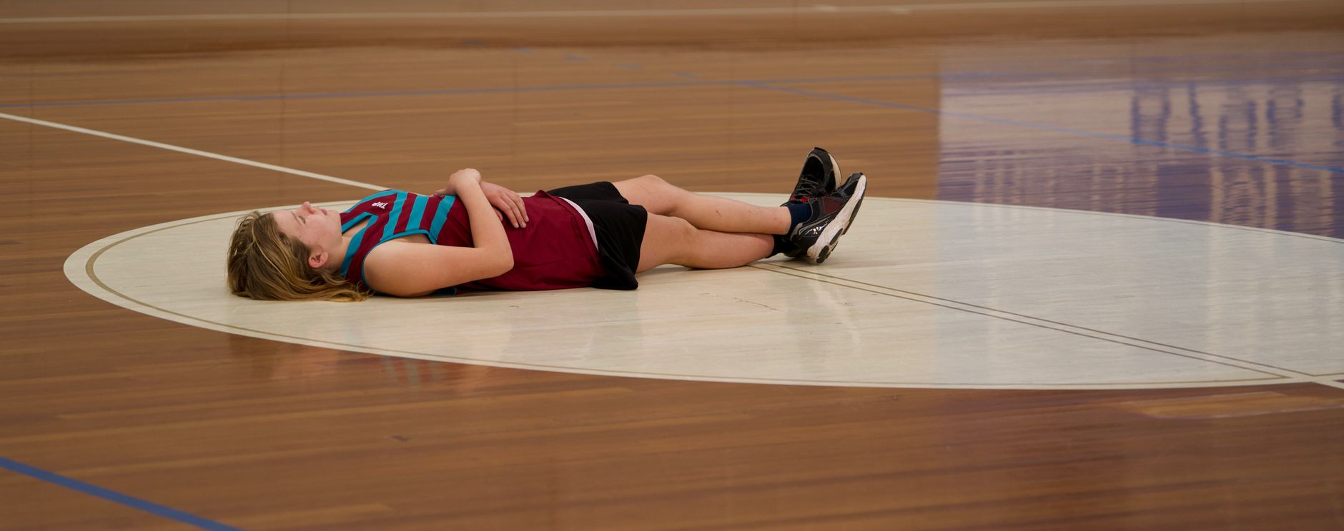 A young female basketball player lies on a court, capturing a moment of rest.