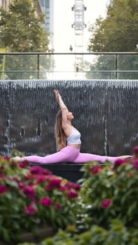 A woman practicing yoga near an urban waterfall in a Sydney park, showcasing flexibility and tranquility.