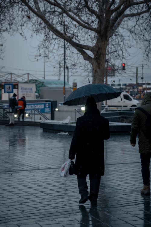 Free City scene with people walking under umbrellas on a rainy day, reflecting on wet pavement. Stock Photo