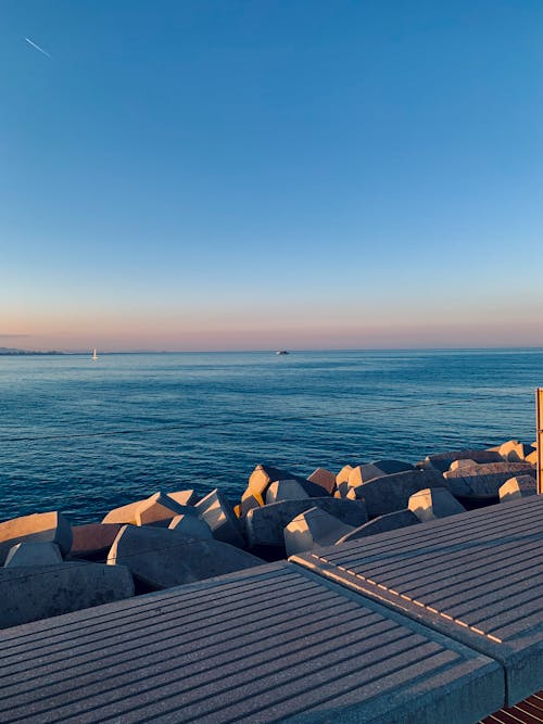 View of a Concrete Pier and Stones on the Shore at Sunset