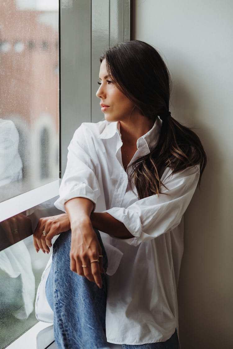 Woman In A White Shirt Sitting And Looking Through The Window 