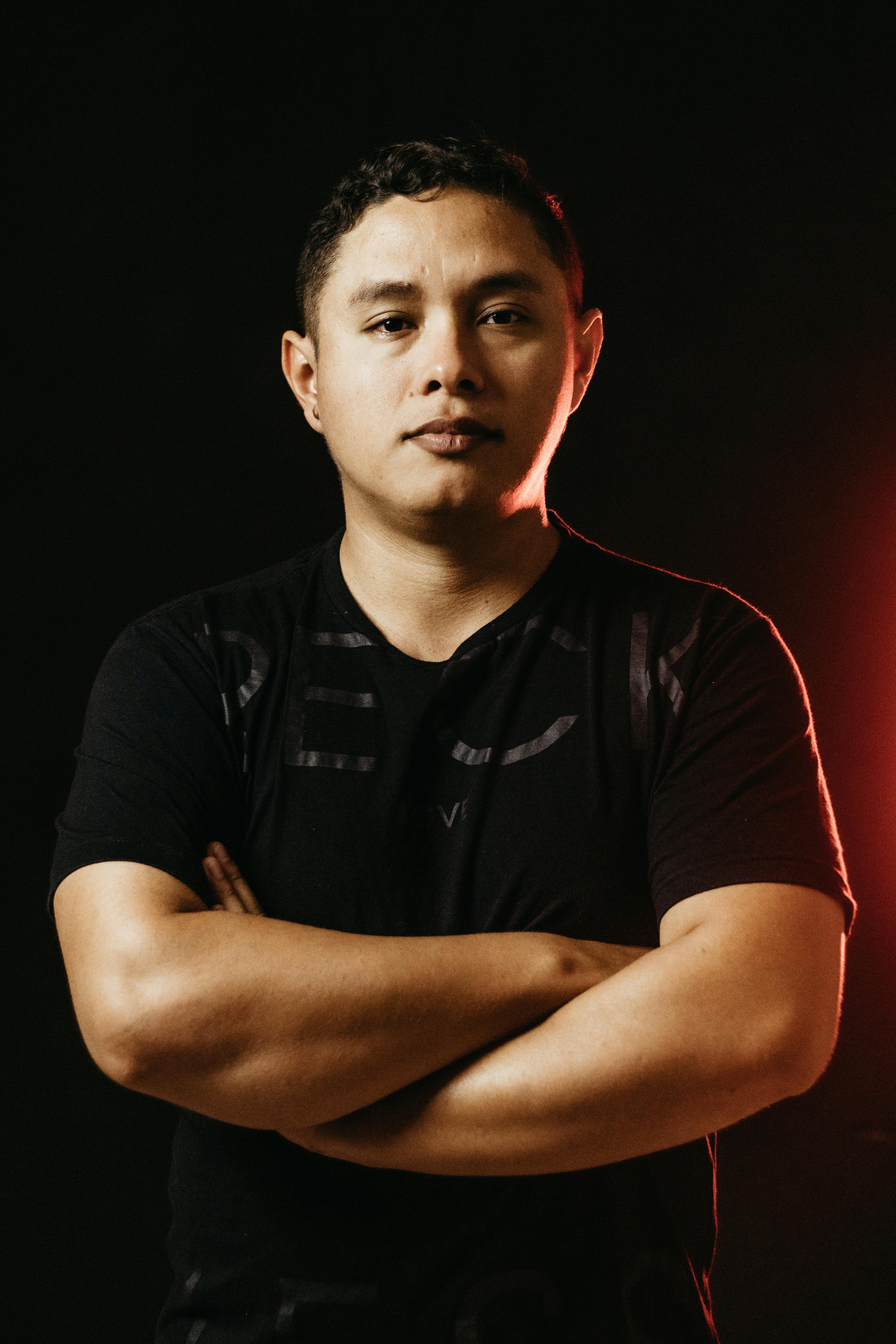 Studio portrait of a confident man with crossed arms and red backlighting, conveying strength.
