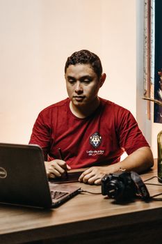 Adult man focuses on digital work using a laptop and tablet, DSLR camera nearby.