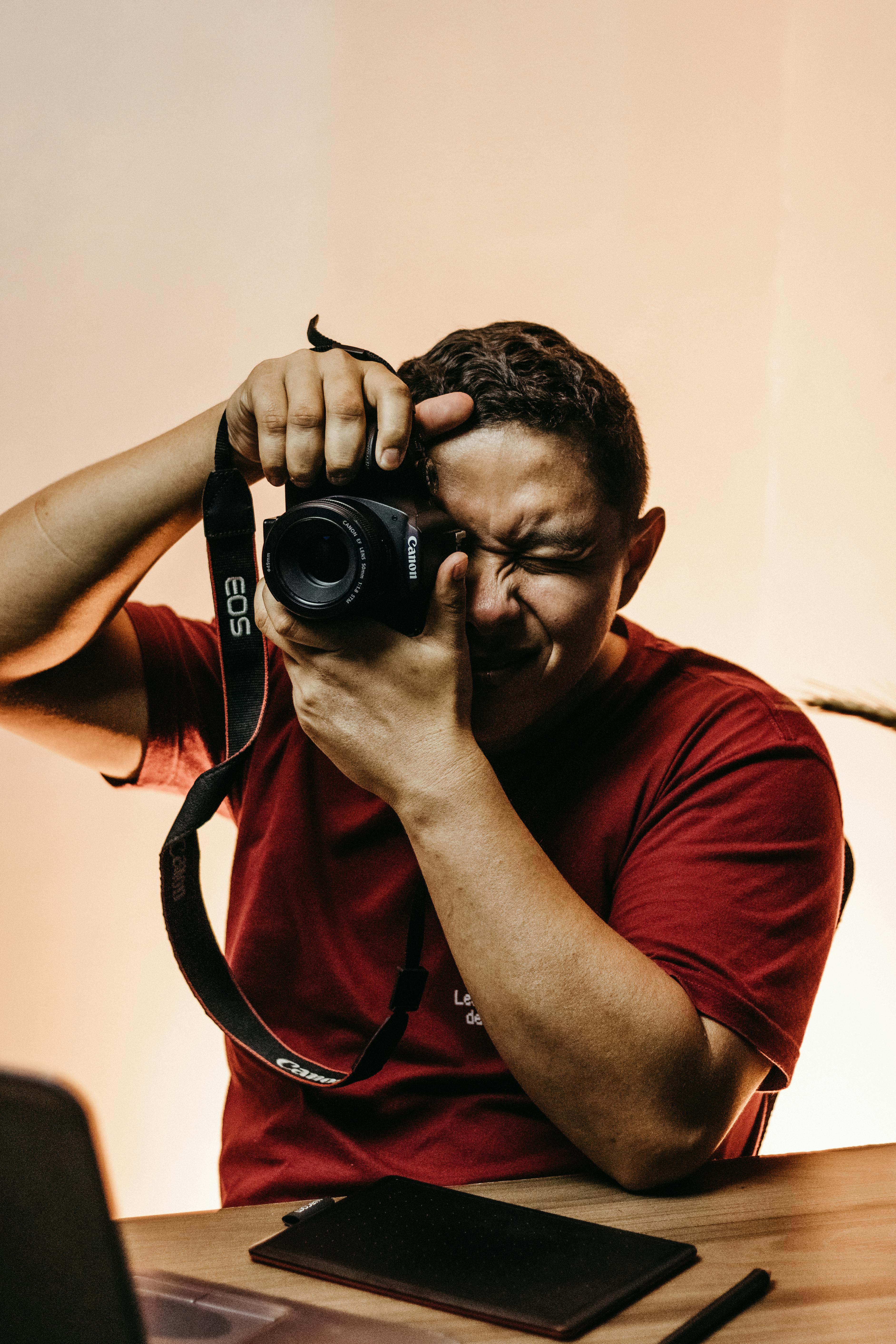 Man in red shirt taking a photo with Canon EOS in a well-lit indoor setting.