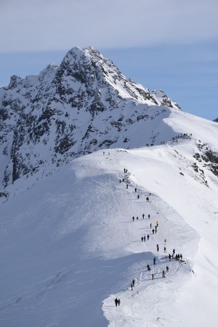Group of hikers traversing a picturesque snowy mountain ridge under clear skies.