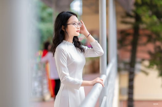 A woman in a white traditional Vietnamese dress poses elegantly outdoors beside a railing.