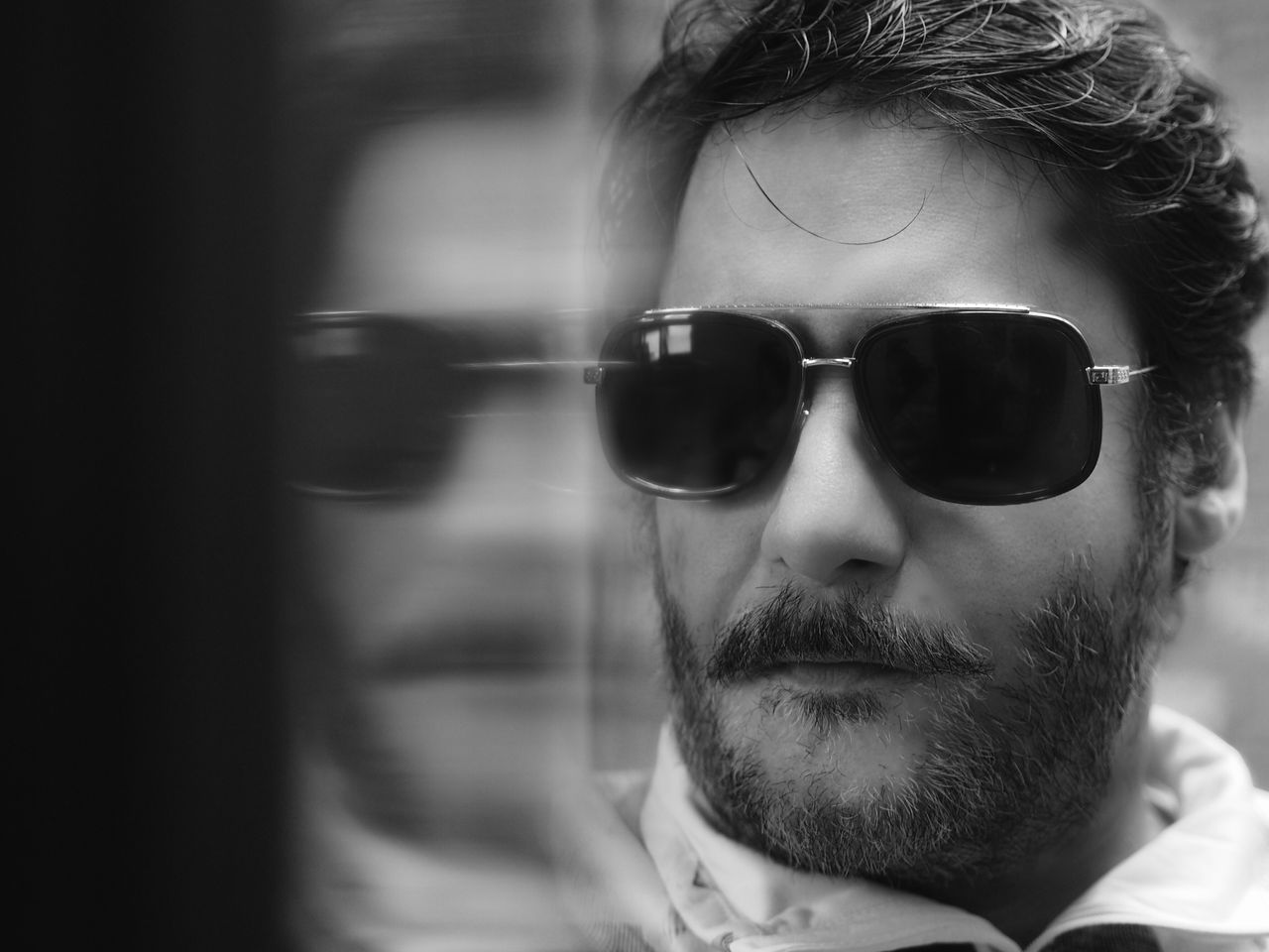 black and white portrait of a man wearing sunglasses reflected in glas