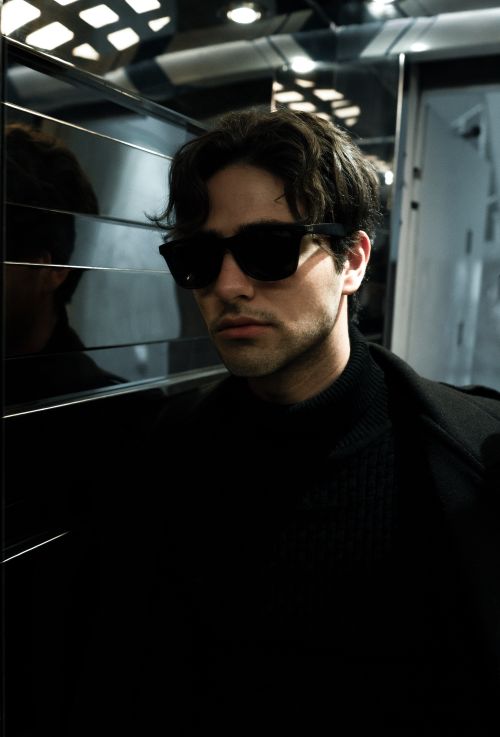 Free Portrait of a fashionable young man wearing sunglasses, posing in a sleek, modern environment. Stock Photo