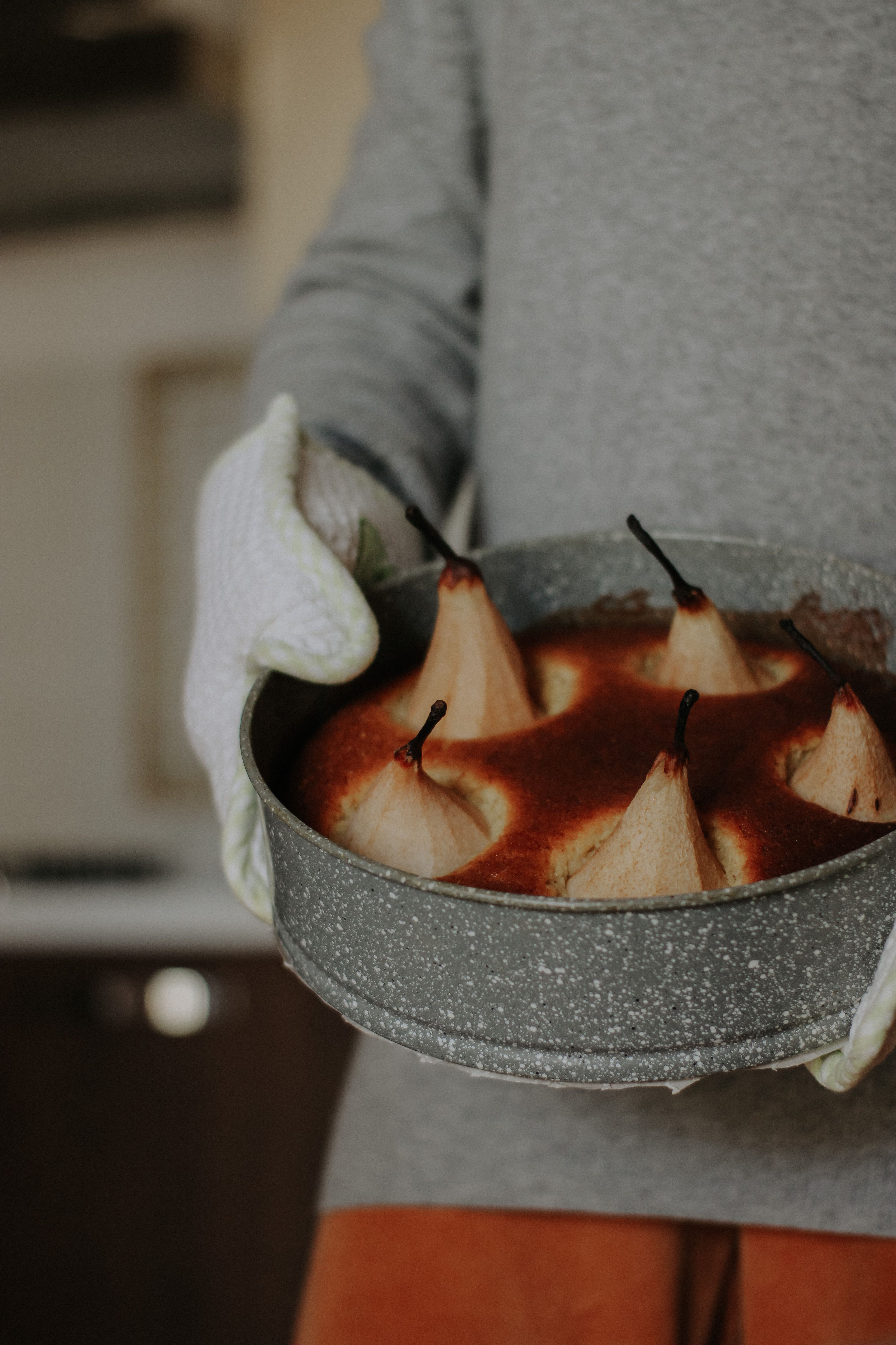 A close-up view of a baked pear dessert held with oven mitts, showcasing food photography.