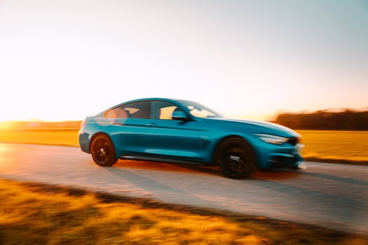 Vibrant blue car speeding on an open road during a serene sunset.