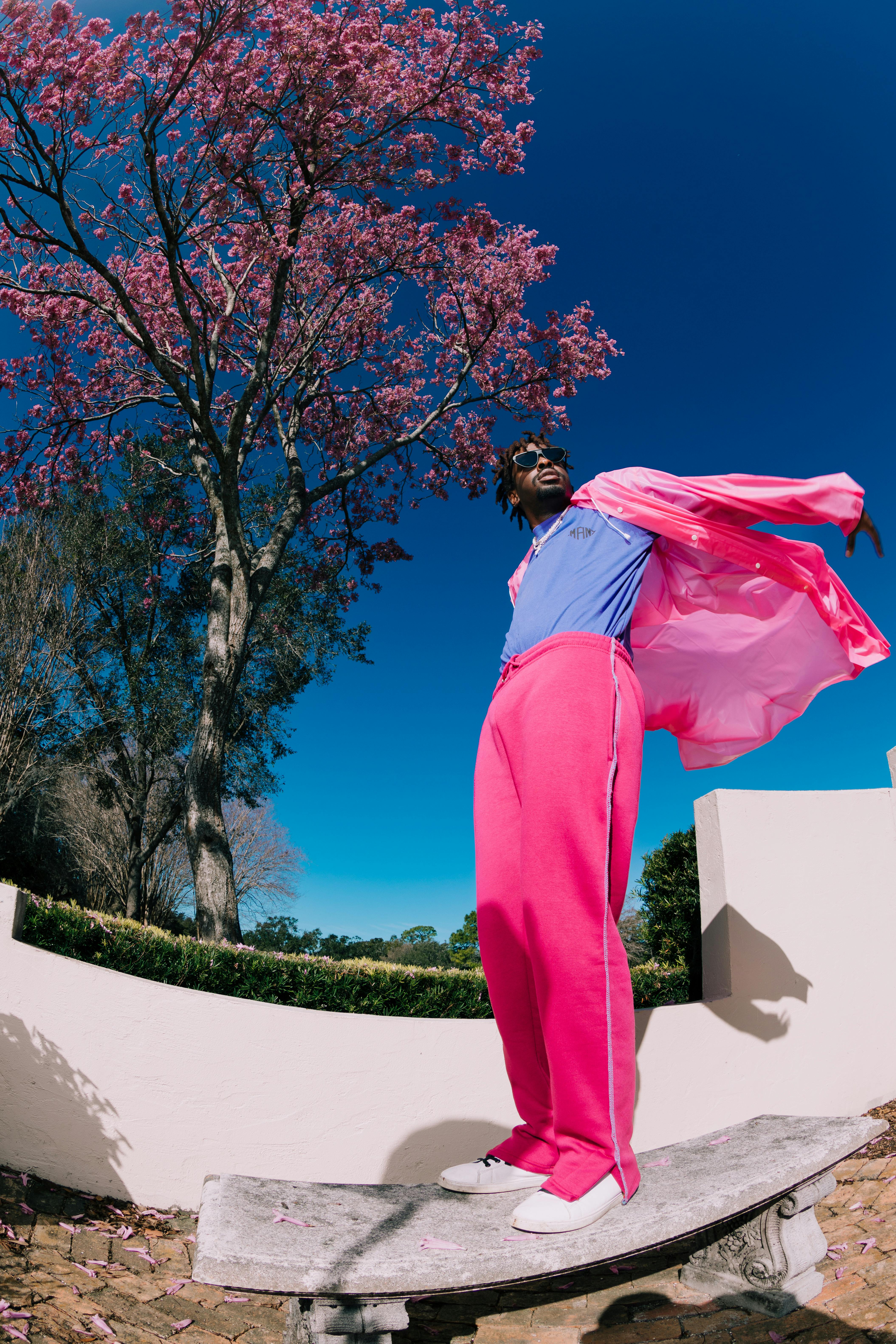 A vibrant portrait of a man posing in stylish activewear under a pink blossom tree.