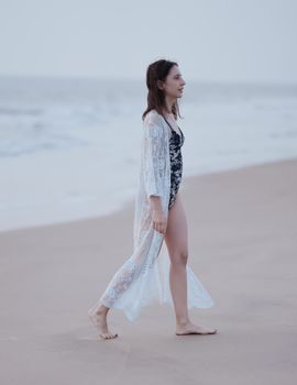 A woman in a stylish lace cover-up walks along a tranquil beach, capturing a serene fashion moment.