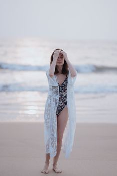 Woman standing by the sea in a floral swimsuit and lace cover-up, exuding calmness.