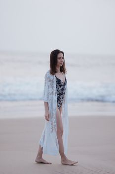 Elegant woman walking on a serene beach in a lace cover-up at dusk.