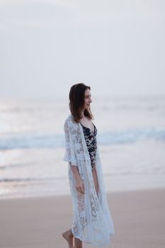 A woman in stylish beachwear standing gracefully on a tranquil beach at twilight.