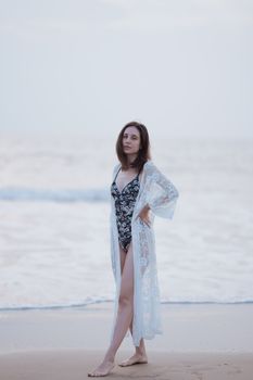 Woman in a lace cover-up posing confidently on a serene beach amidst calming waves.
