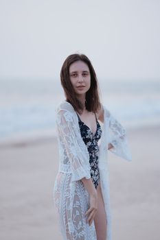 A woman in stylish lace attire poses gracefully at the beach with a soft seaside background.