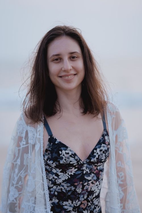 Free A smiling woman with long hair stands on a beach wearing a floral dress and lace cover-up. Stock Photo