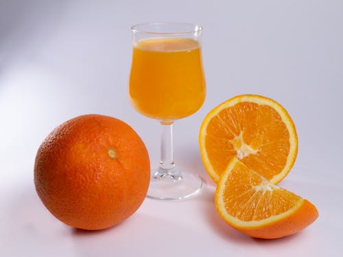 Close-up of Fresh Orange Juice in a Glass and Oranges Lying on White Surface