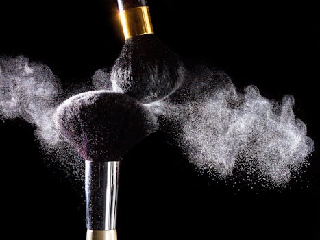 High-speed capture of makeup brushes dispersing powder against a black background.