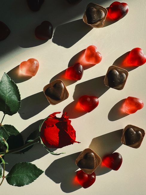 Heart-shaped chocolates and gummy candies with a red rose create a romantic setting.