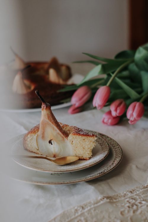 Free A slice of pear cake elegantly presented with tulips, creating a cozy dining atmosphere. Stock Photo
