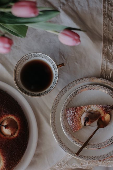 Stylish top view of coffee, cake slice, and pink tulips on a rustic table setting.