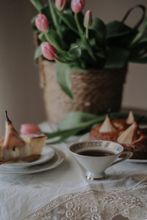 Free A cozy tea setting with tulip flowers, pear cake, and a cup of coffee on a lace tablecloth. Stock Photo