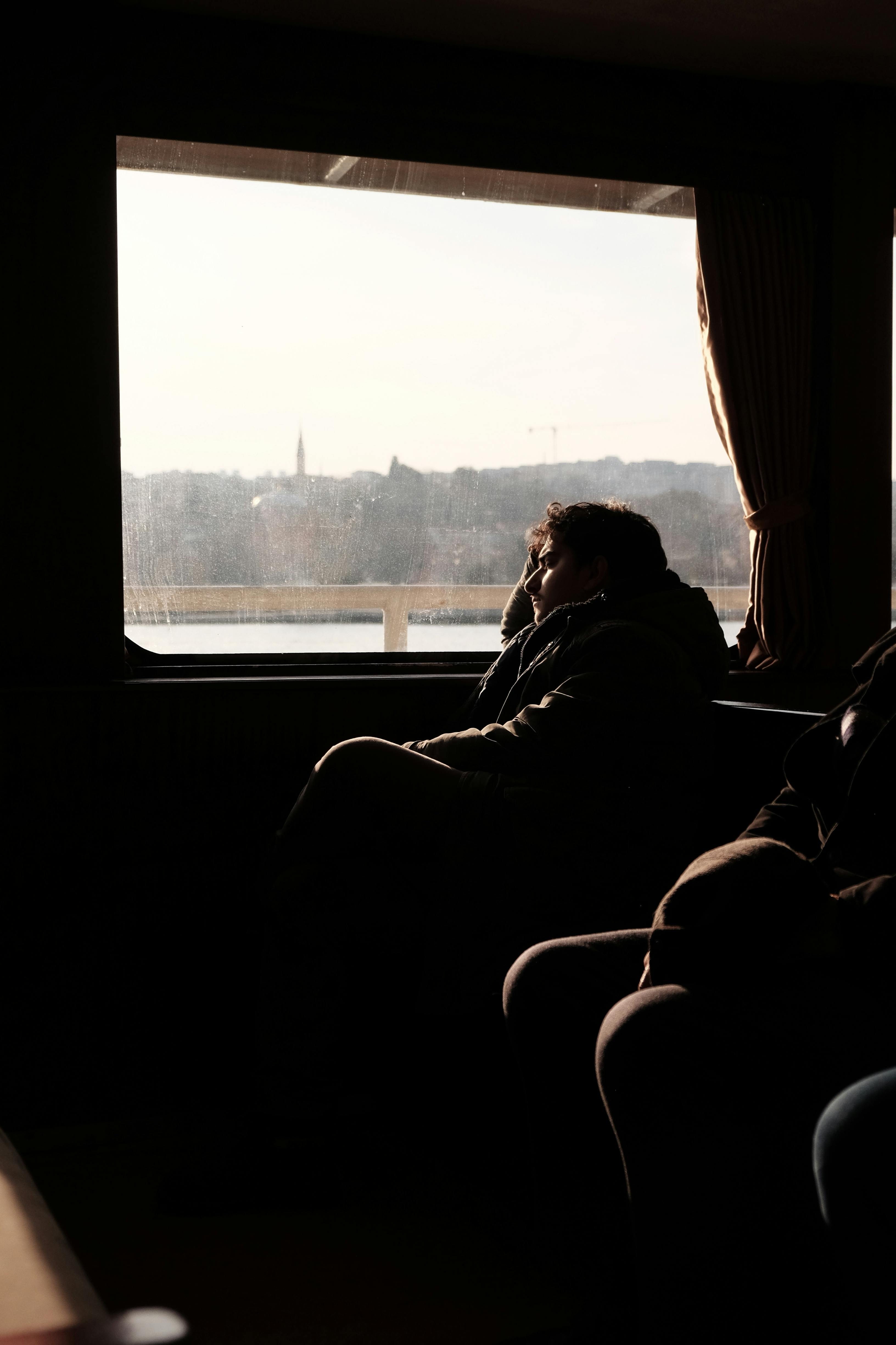 Person gazing out ferry window at distant shore, capturing a moment of reflection during travel.