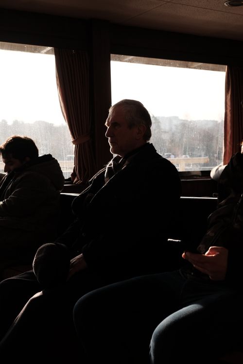 Free Silhouetted passengers relax inside a cozy ferry, enjoying the serene view through large windows. Stock Photo