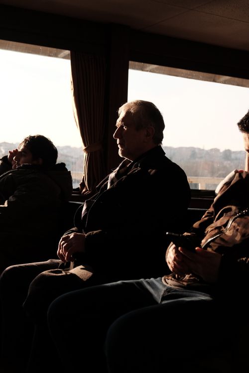 Free Elderly man sitting on ferry with others during sunset, highlighting window views. Stock Photo