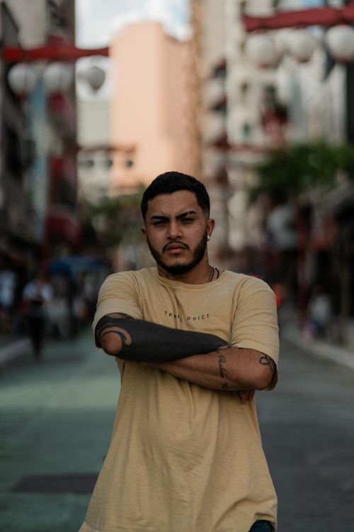 Free Portrait of a man with tattoos standing confidently on a vibrant urban street. Stock Photo
