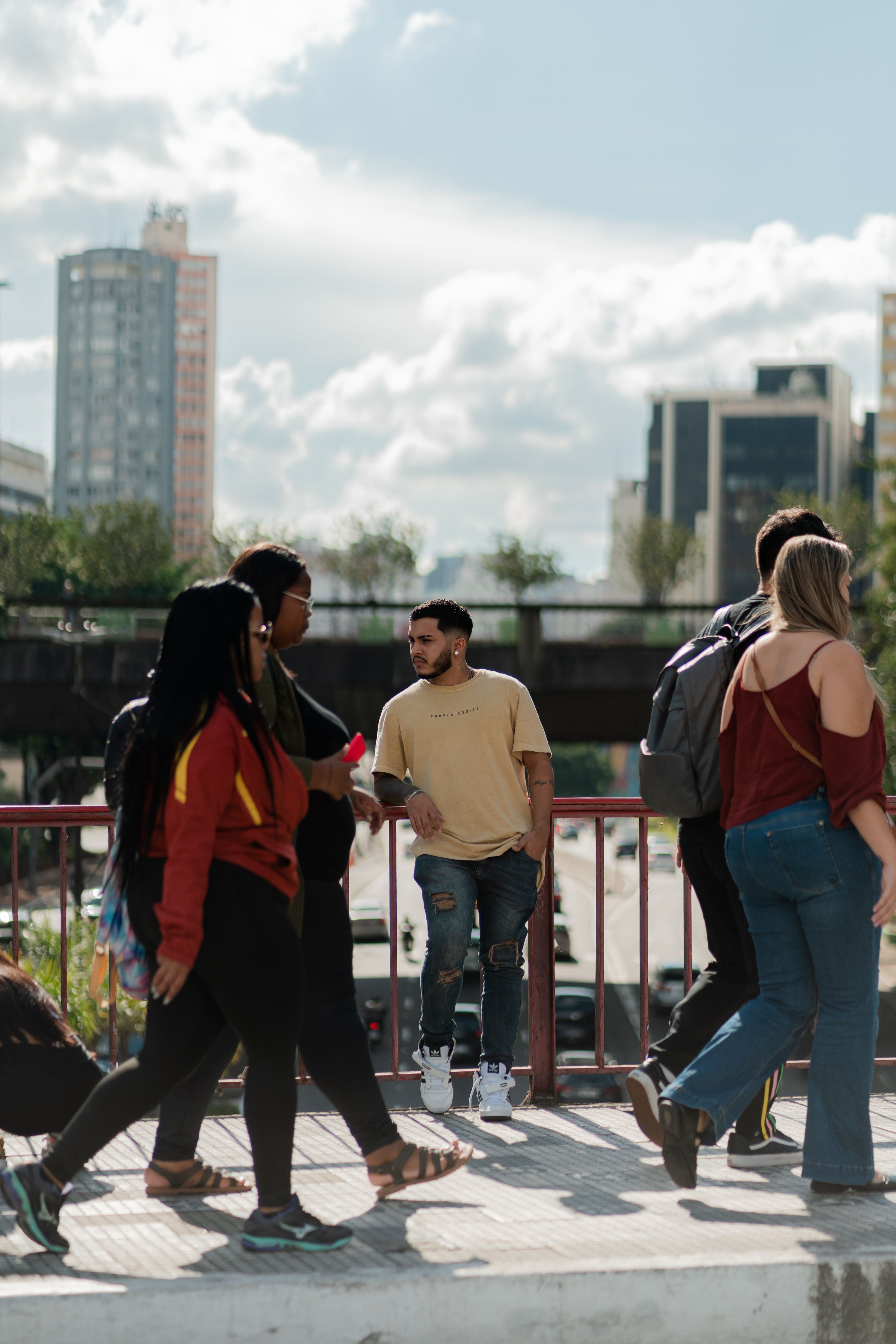 A diverse group of people walking on a city bridge on a sunny day.