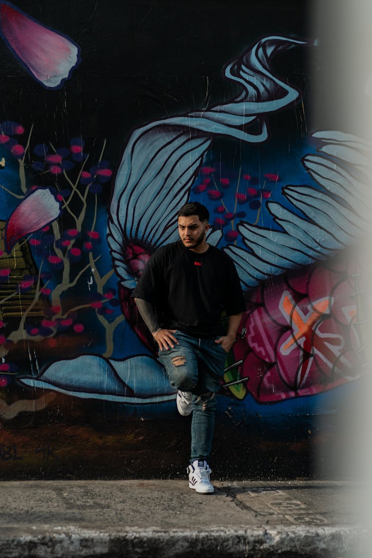 Man Standing And Leaning Against A Wall With A Mural On It 