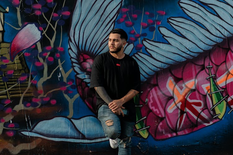 Man Leaning Against A Wall With A Mural On It 