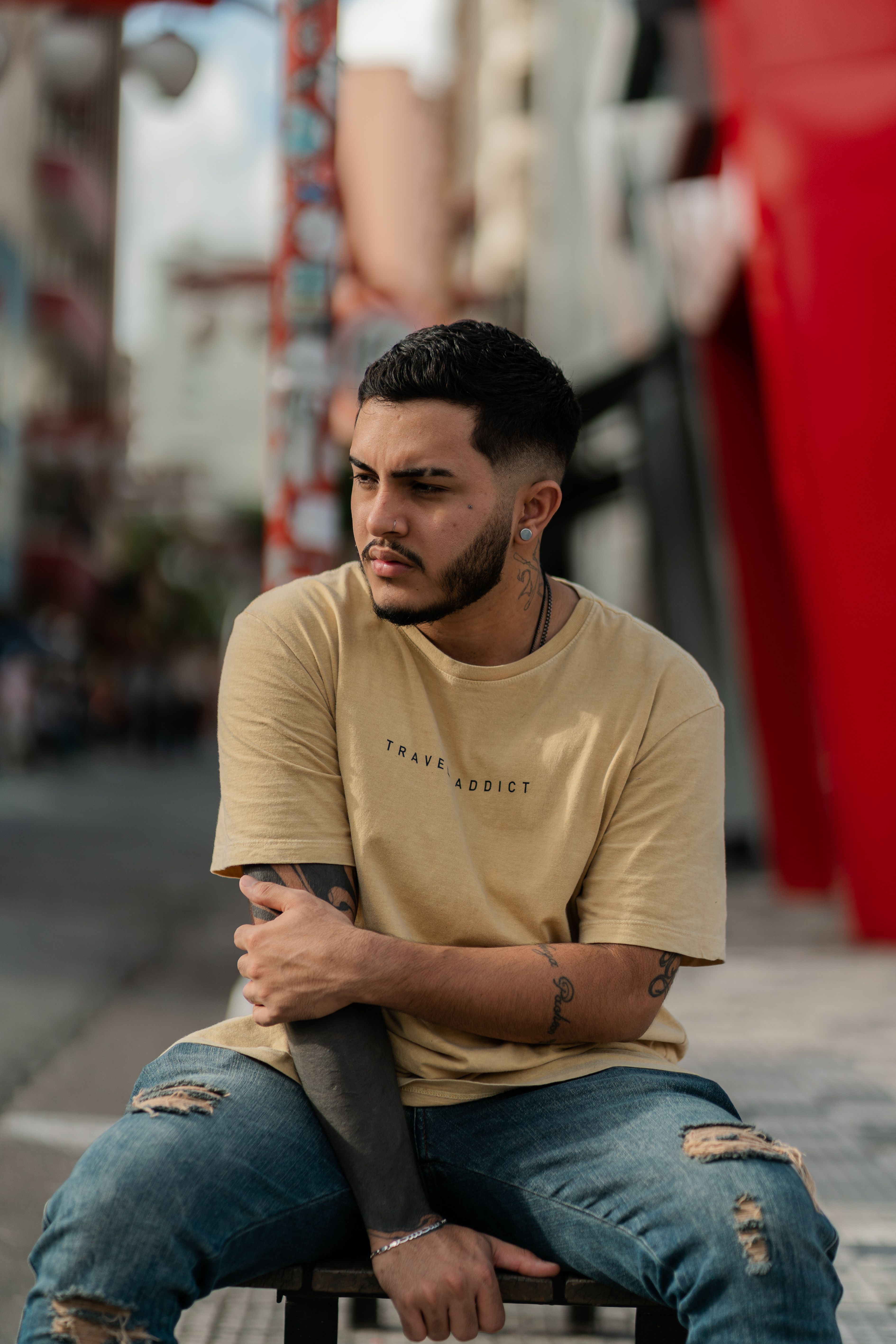 A man in a t-shirt and ripped jeans sitting outdoors, showcasing casual urban style.