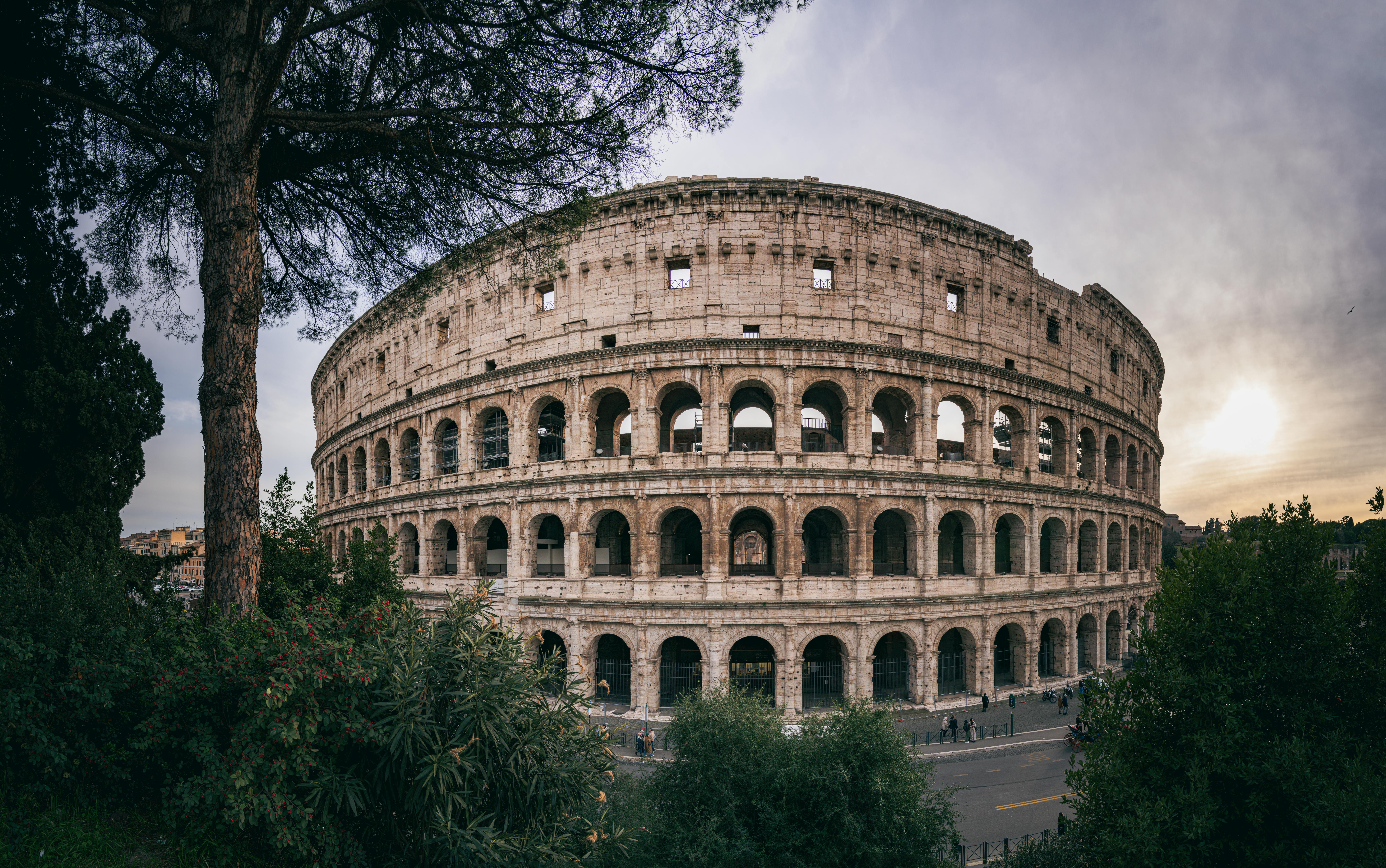A family with two children standing in front of the illuminated Colosseum at dusk, smiling and pointing.