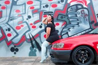 一位时尚女性倚着充满活力的涂鸦墙，在一辆红色汽车旁摆姿势