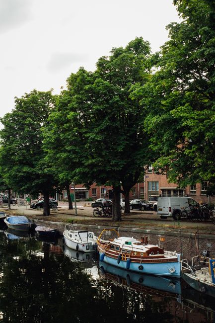 A serene canal with docked boats and lush trees in an urban setting.